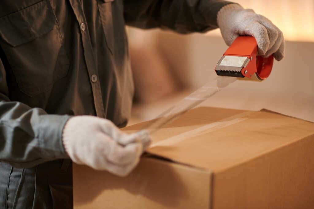 Cropped image of a professional packer sealing a cardboard with adhesive in the concept of 'what are the benefits of hiring professional packers'.